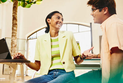 Man and woman sitting at table having a chat, while woman working on a tablet.