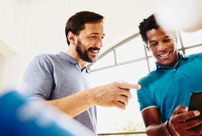 Two smiling colleagues (men) looking at a phone.