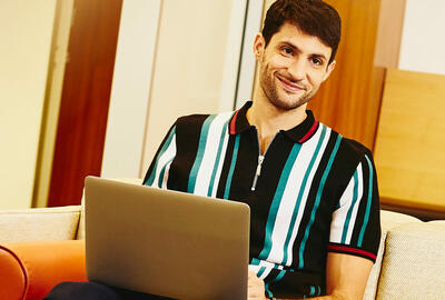 Man sitting on couch working on laptop. 