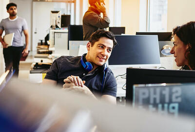 Smiling man with headphones having a conversation at his desk.