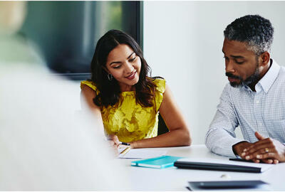 Man and woman sitting down, both looking at paperwork.