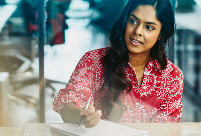 Woman working in an office, sitting at a table making notes.