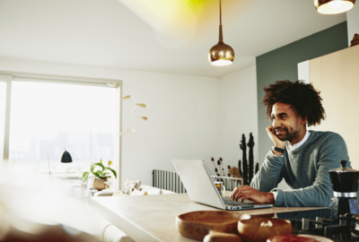 Man leaning against the counter top, while working on laptop.