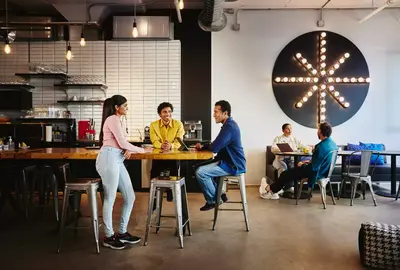 2 male sitting at a table and a female standing at the table and two people sitting at another table