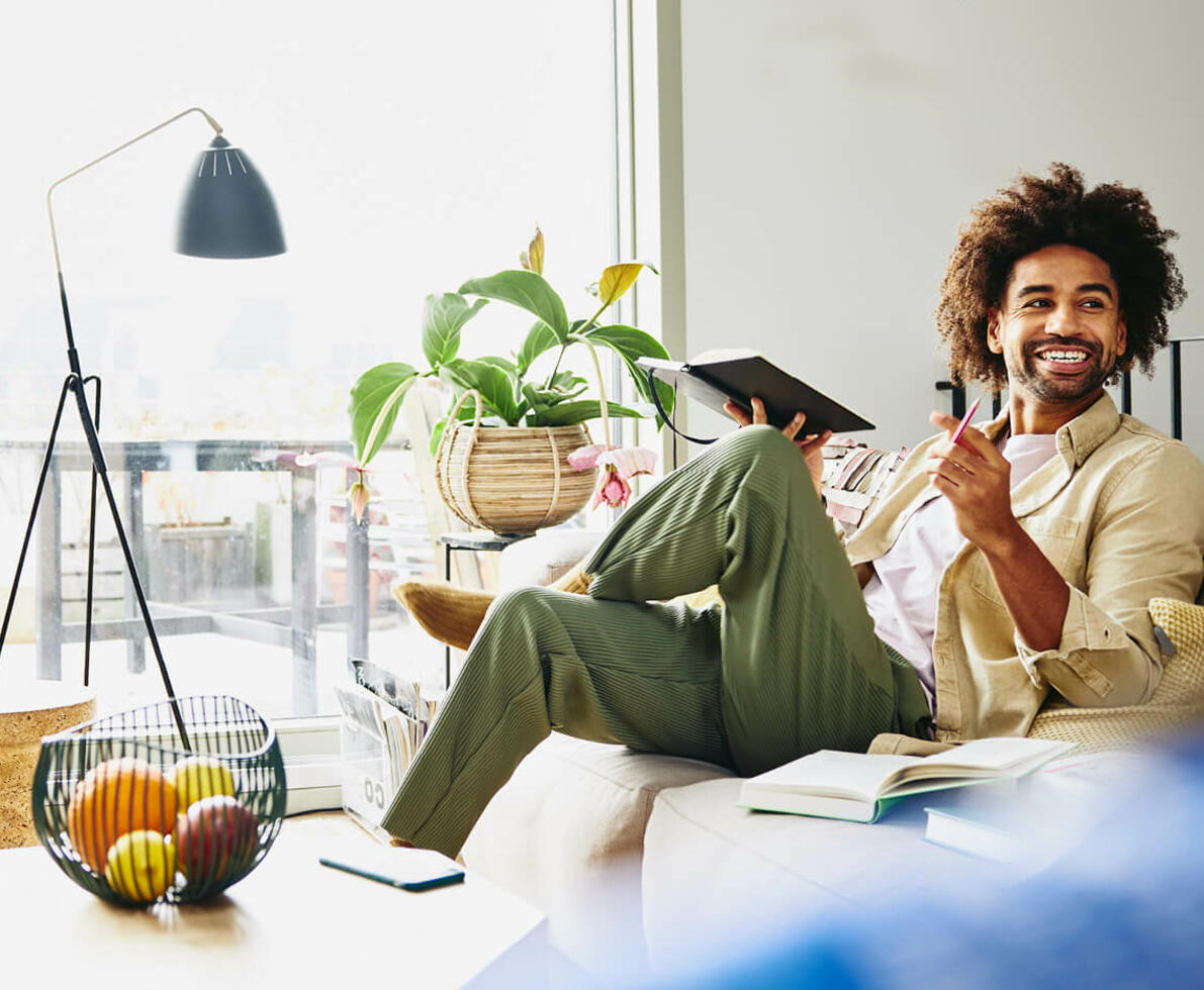 Smiling man sitting on a couch holding a notebook and a pen.