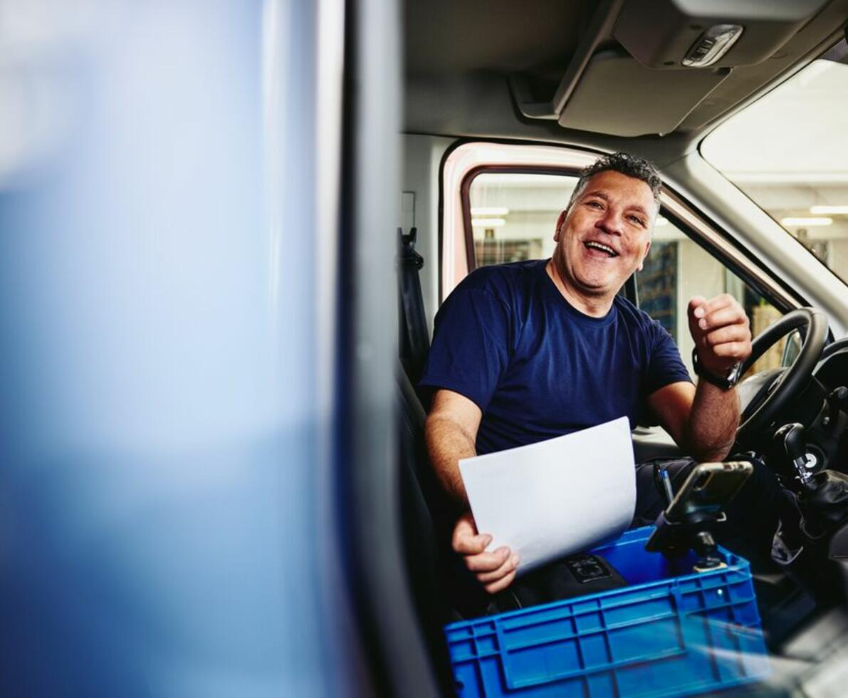 Smiling man sitting in driver's seat of a logistics truck holding a piece of paper