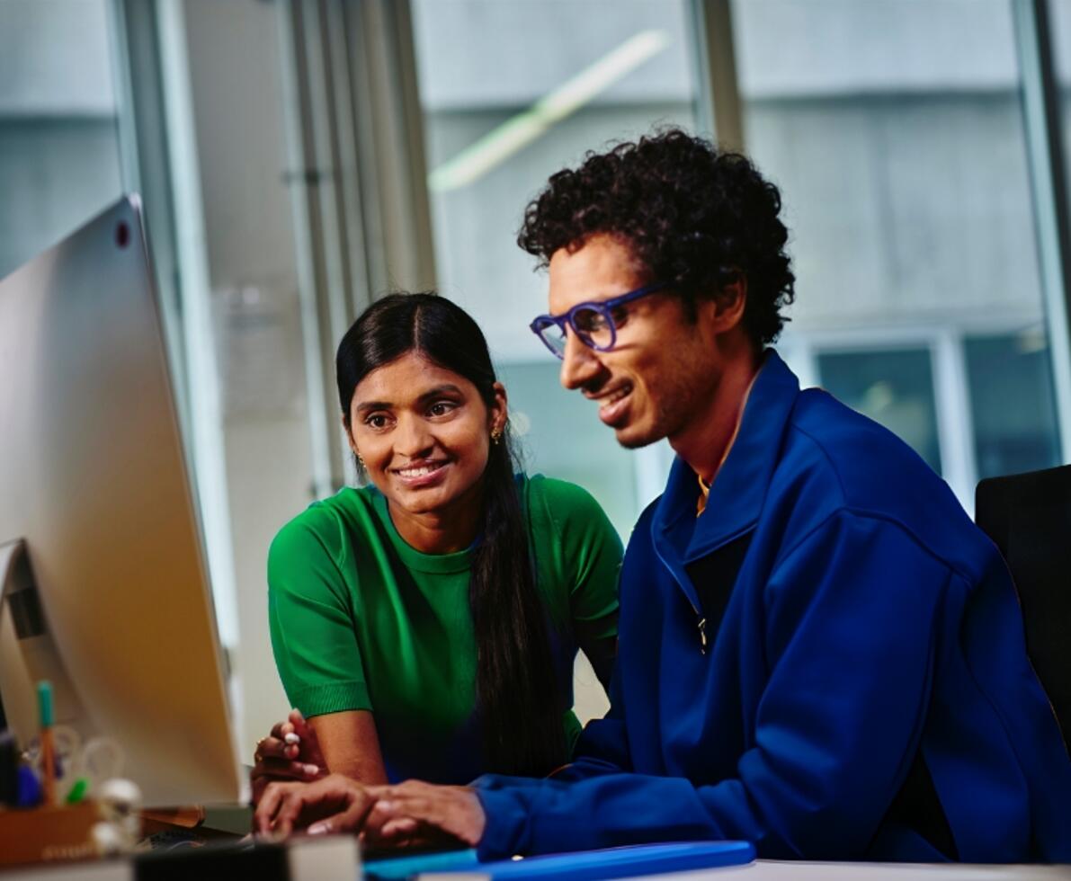 an image of two coworkers smiling while looking at something on the monitor
