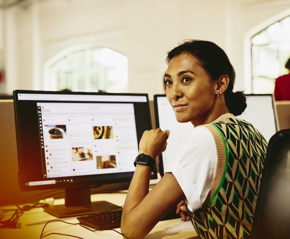 Woman sitting at her desk, looking away from computer screens displaying marketing content.