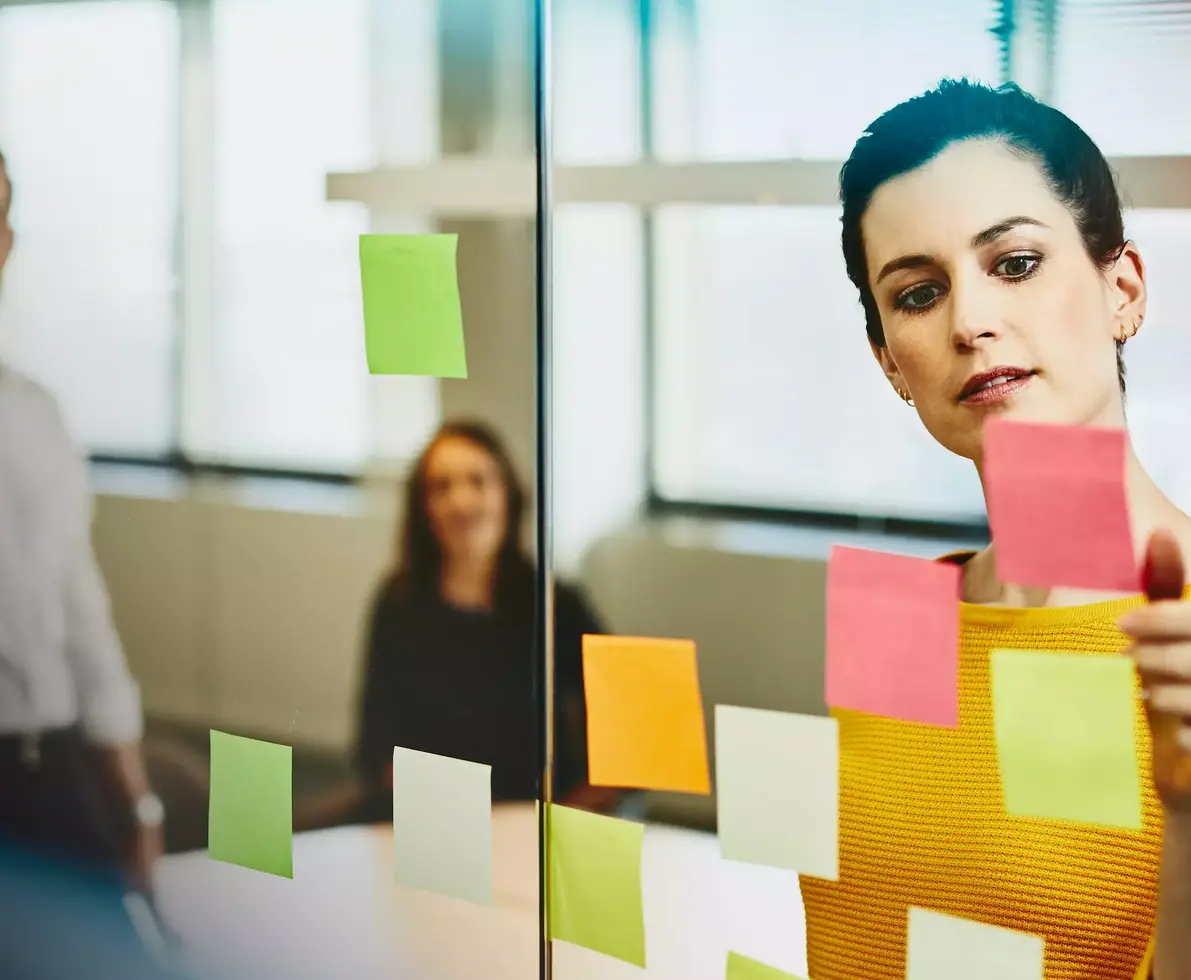 Two business female and a male in an office putting sticky notes on a window.
