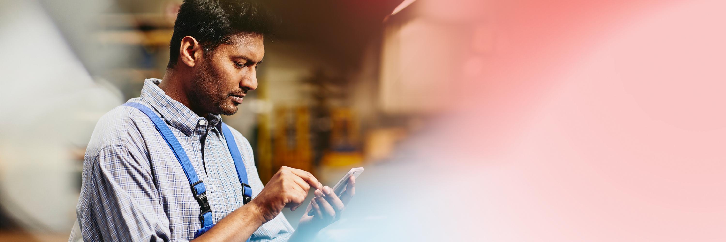 Focused man looking down to phone in production site.