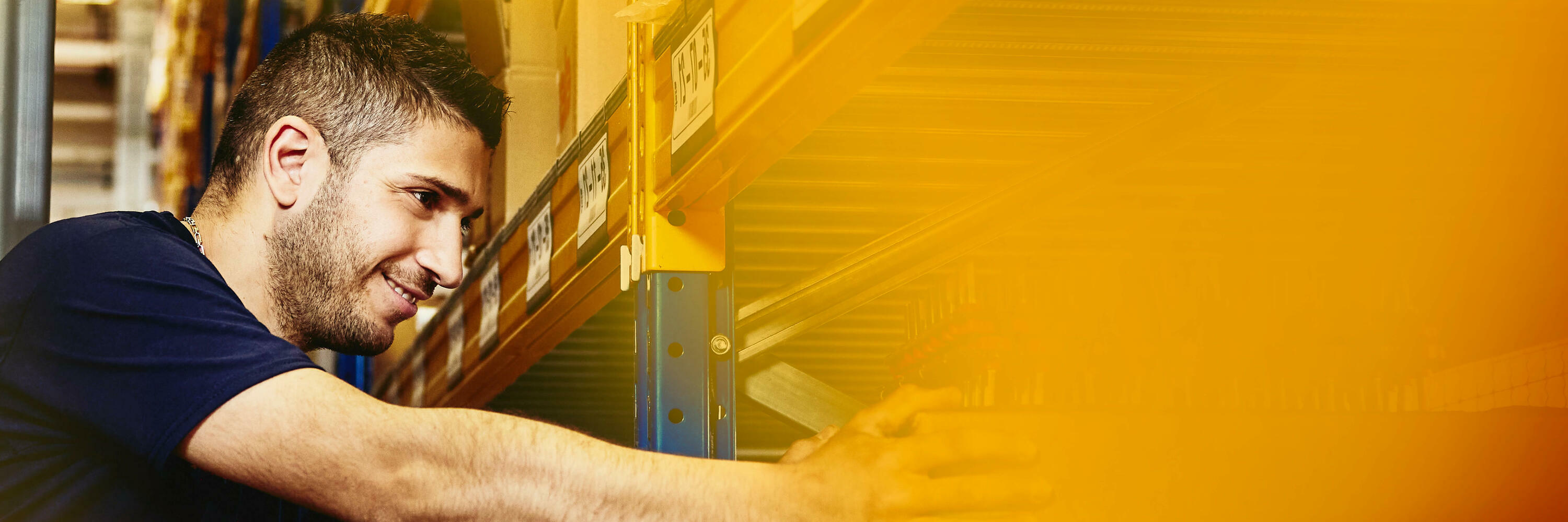 Man in elevator between distribution center racks, picking up a box from a shelf