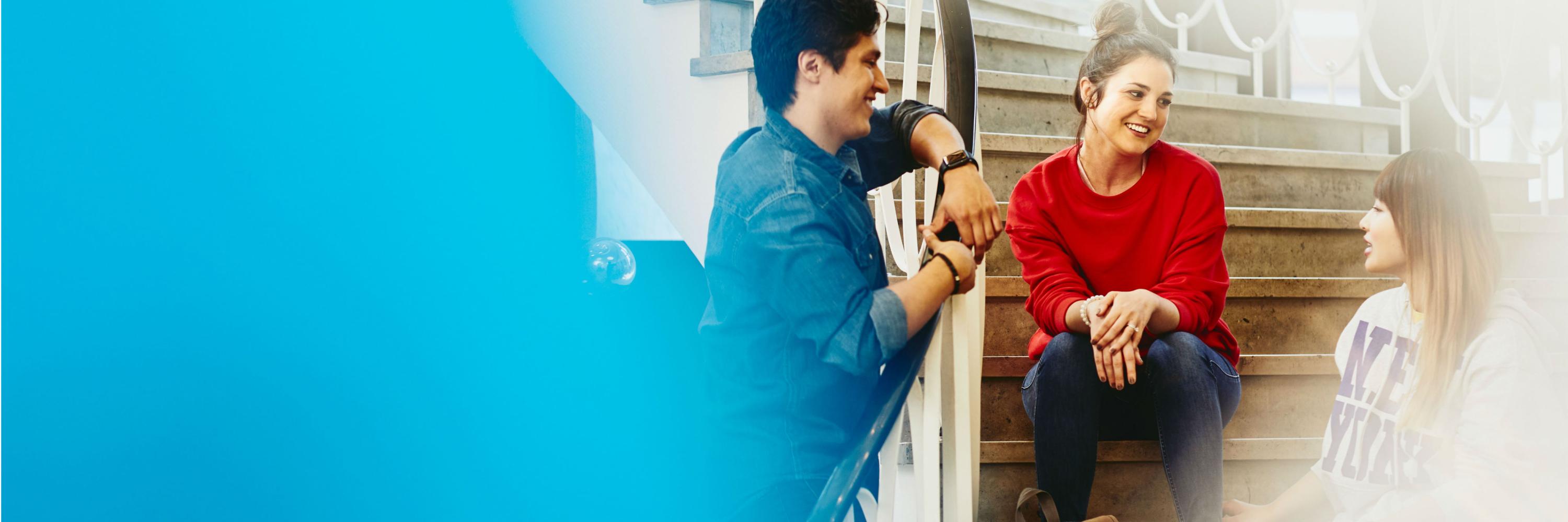 Students sitting on stairs, one student standing next to the stairs. Smiling and having a conversation.