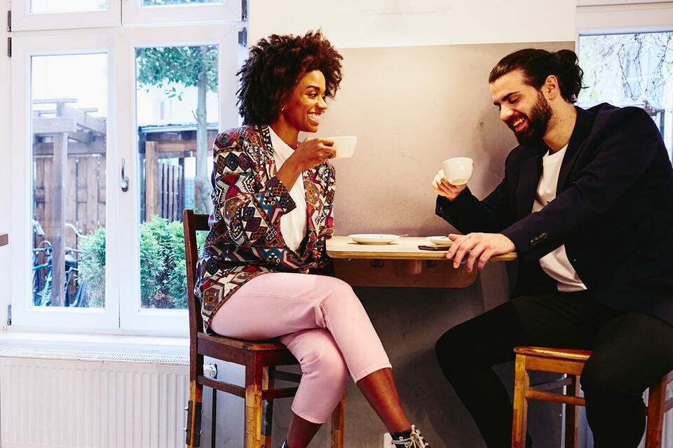 man and woman smiling and talking in a cafe