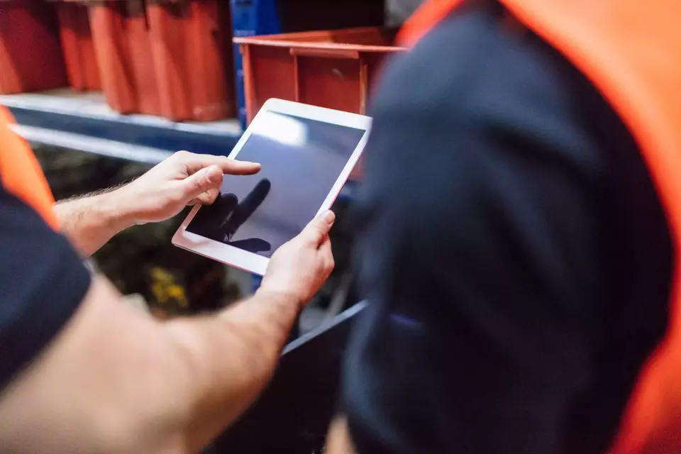 Close up of two workers using tablet computer at factory warehouse. Foremen with colleague using digital tablet in warehouse.