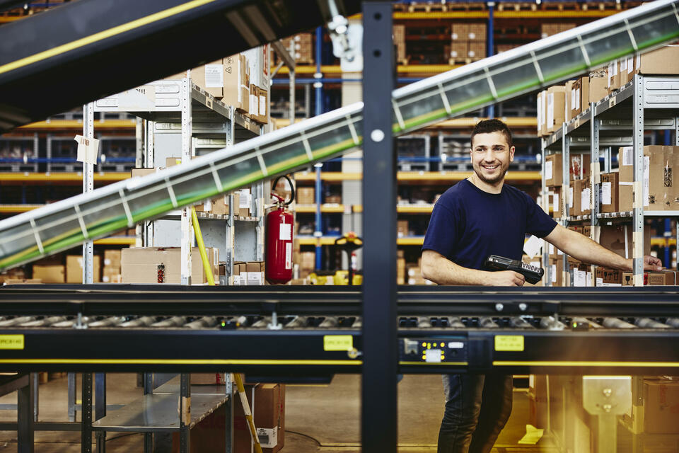 Smiling male standing behind a conveyor belt 
