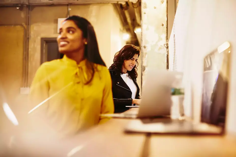 Two smiling female working on their laptop.
