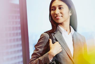 Business woman carrying her bag smiling, city in the background.